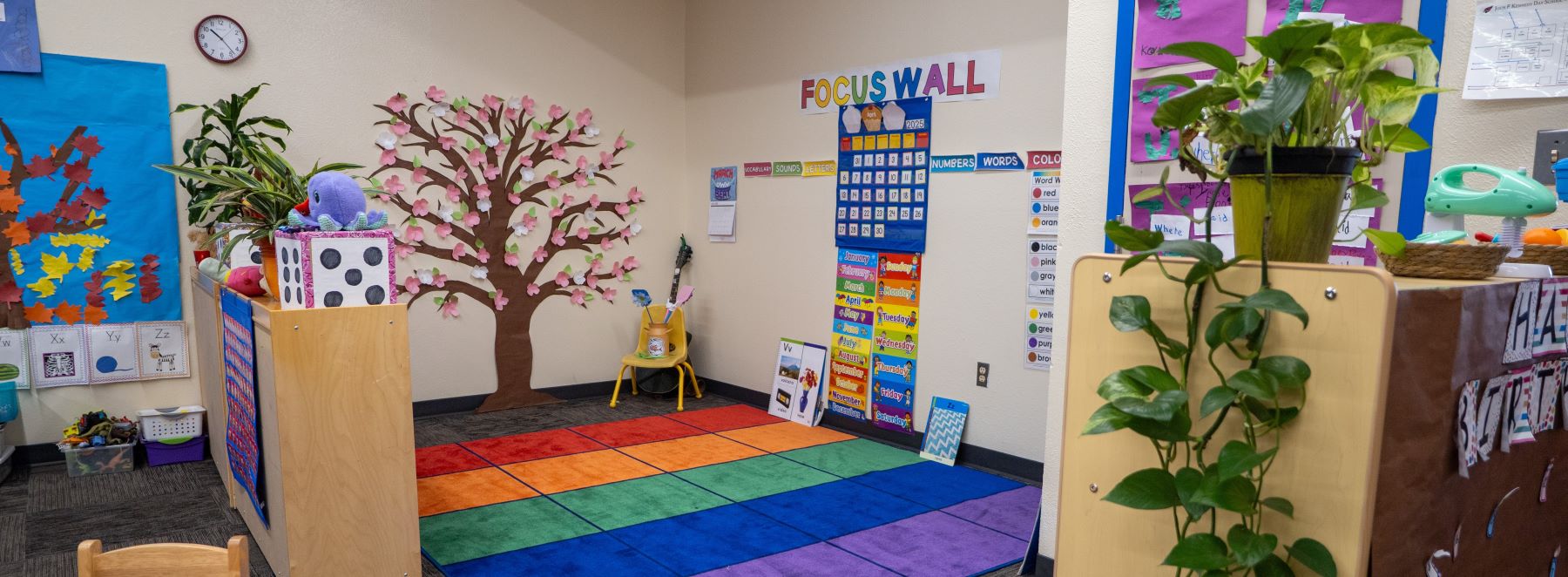 A vibrant classroom featuring colorful floor mats and a decorative tree in the corner, creating a cheerful learning space.