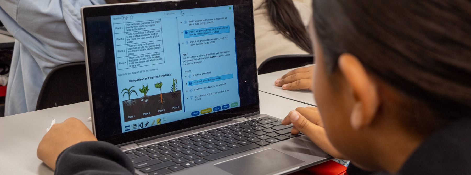 A student focused on a laptop while seated at a desk in a classroom setting.
