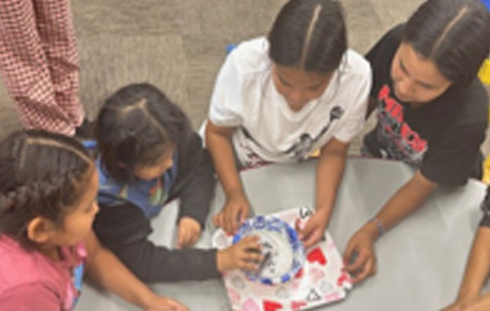 Two female sixth-graders work with two female first-grader on a science project.