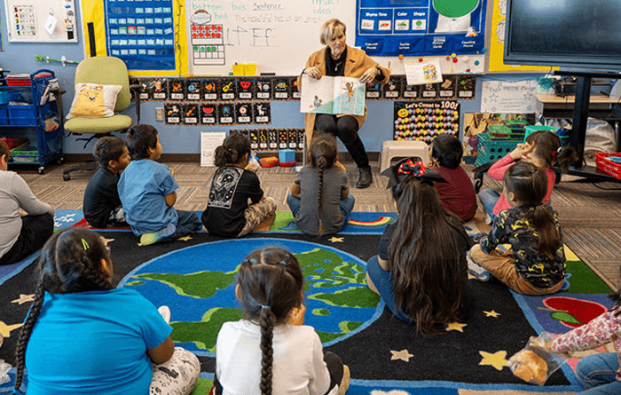 Teacher reading to students who are sitting on the floor in a classroom. 