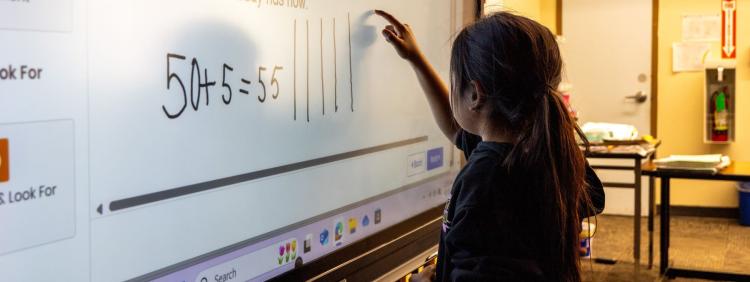 A girl is writing on a whiteboard in a classroom, demonstrating her participation in the lesson.