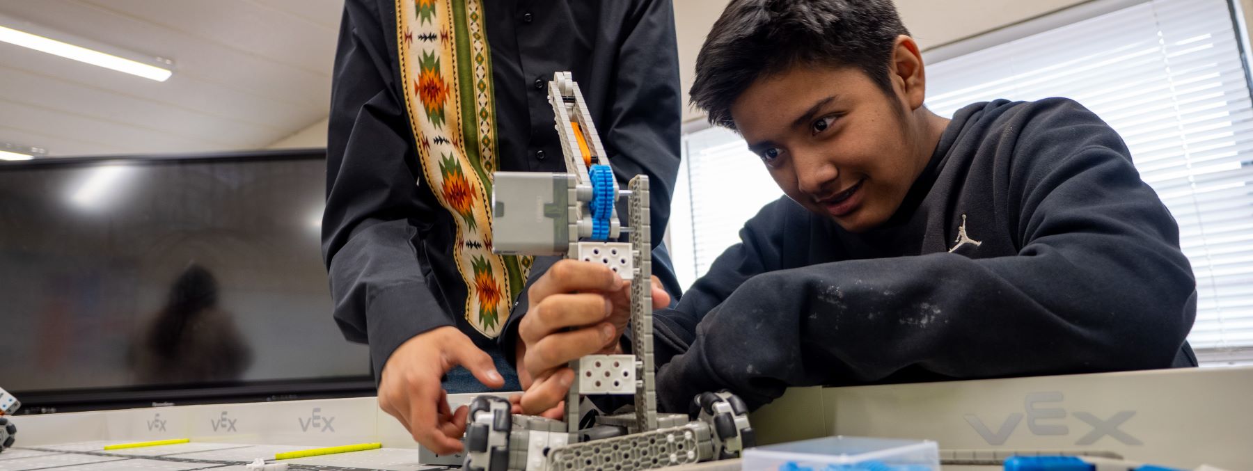 Two young boys collaborate on building a robot in a classroom setting, surrounded by tools and educational materials.