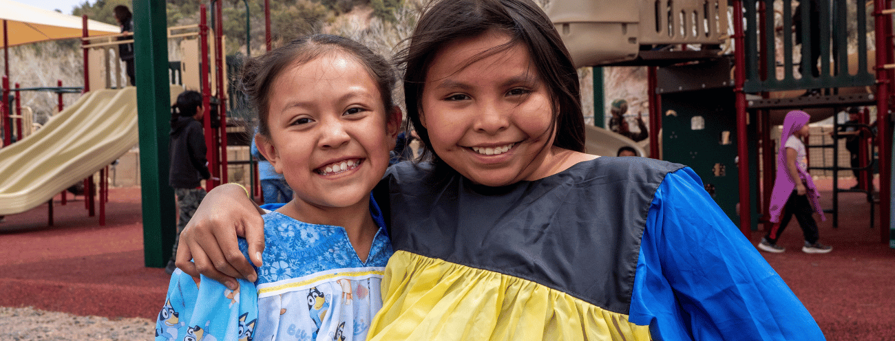 Two young female students standing in front of the school's playground.